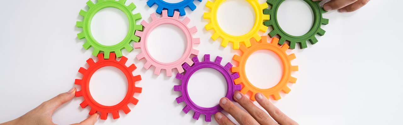 Händer som fogar ihop färgglada plastkugghjul.