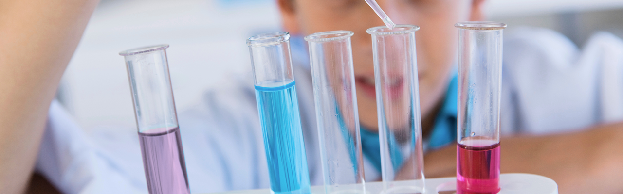 Fem provrör i förgrunden. i bakgrunden syns ett barn som droppar vätska i ett av provrören med pipett.