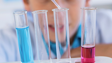 Fem provrör i förgrunden. i bakgrunden syns ett barn som droppar vätska i ett av provrören med pipett.