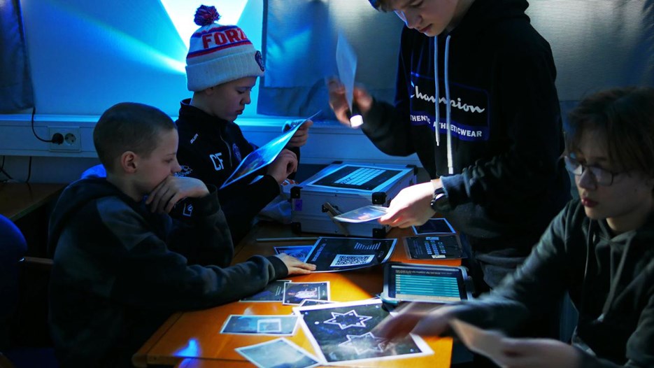 Fyra pojkar undersöker ledtrådar i rymningsspelet Space Escape. 