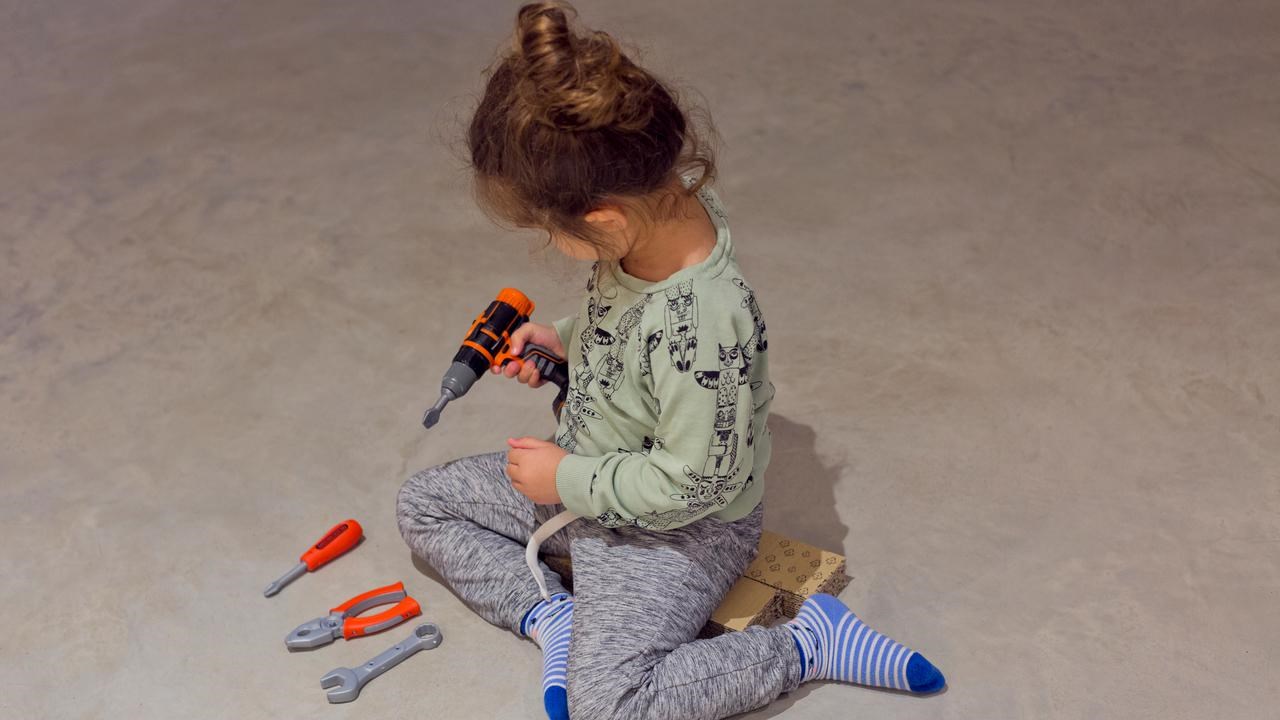 Bild på flicka med leksaksborrmaskin i handen och verktyg på golvet
