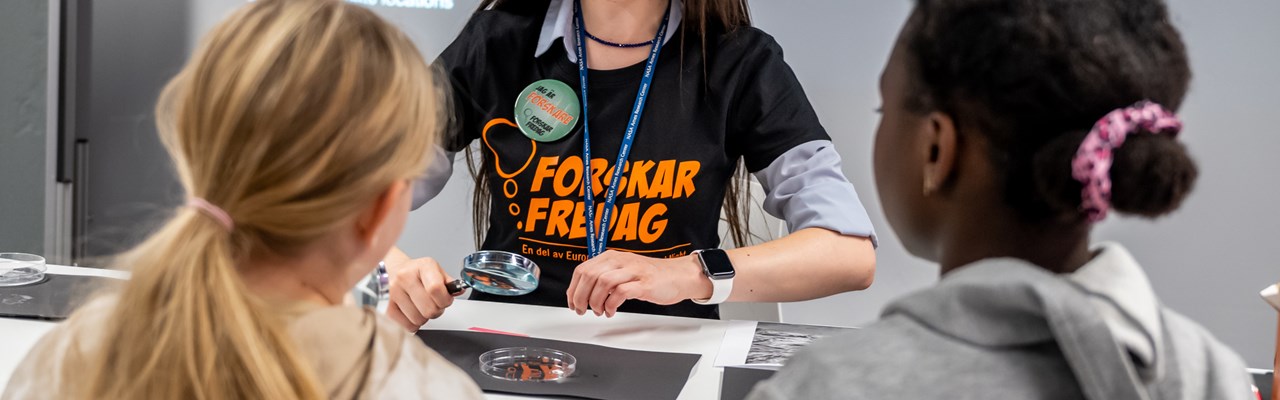 Forskare visar två barn ett experiment med ett förstoringsglas.