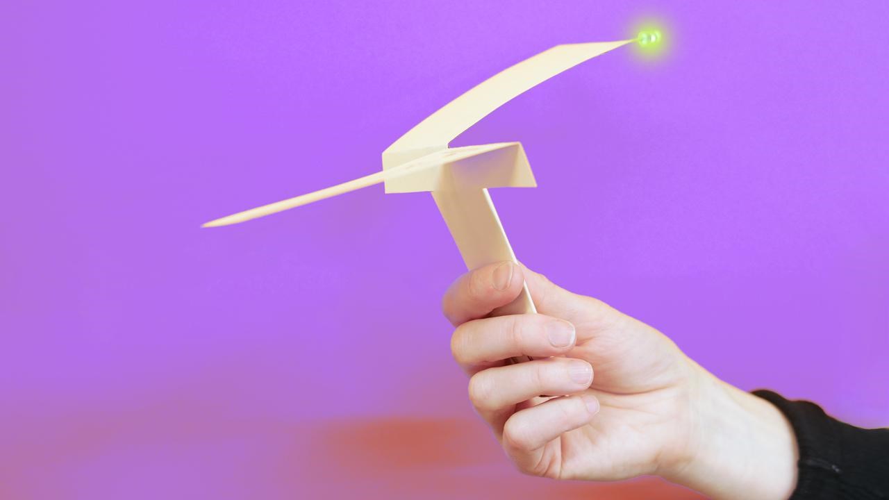Hand som håller i en vikt pappershelikopter med en lysande diod. Lila bakgrund.