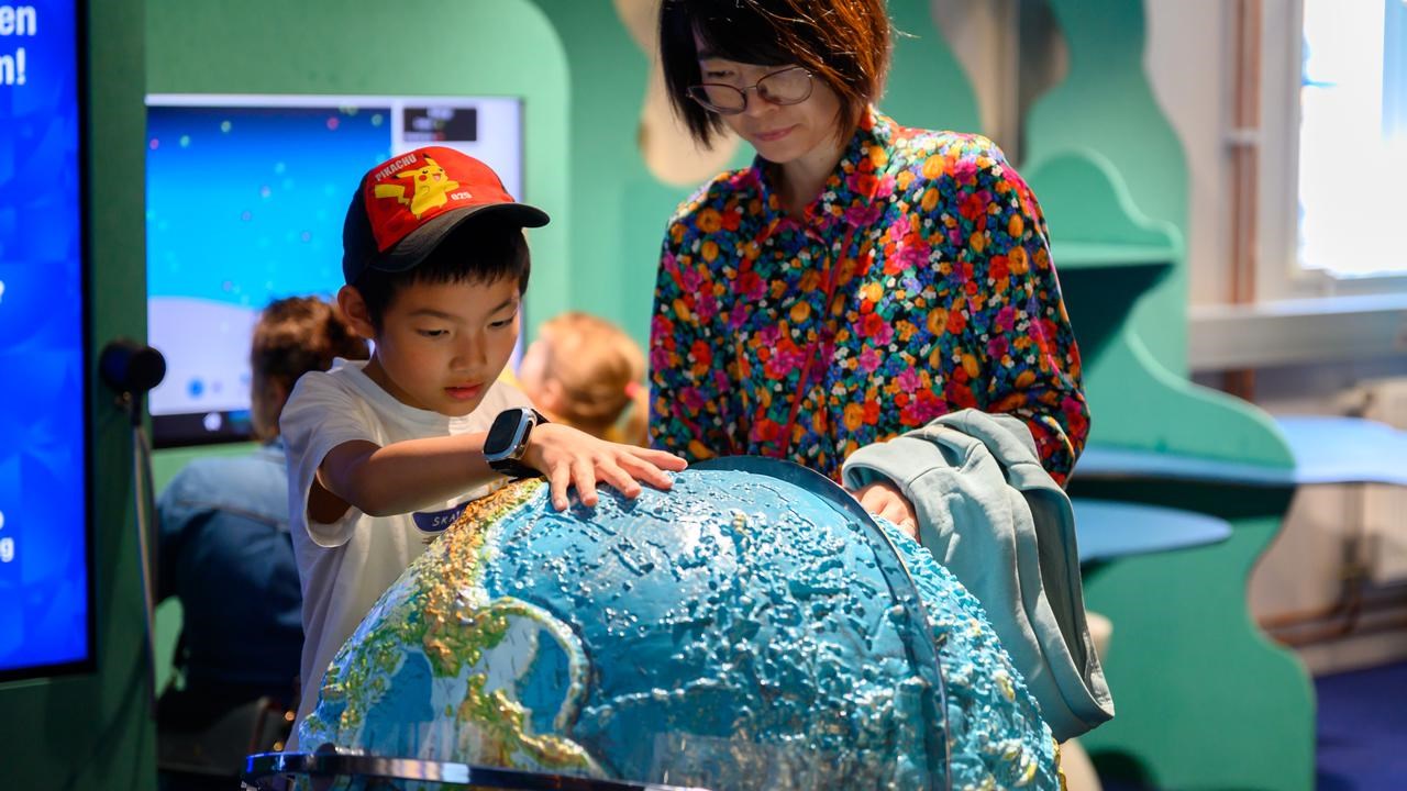 Barn och mamma utforskar jordglob i Curiosums utställning Jorden