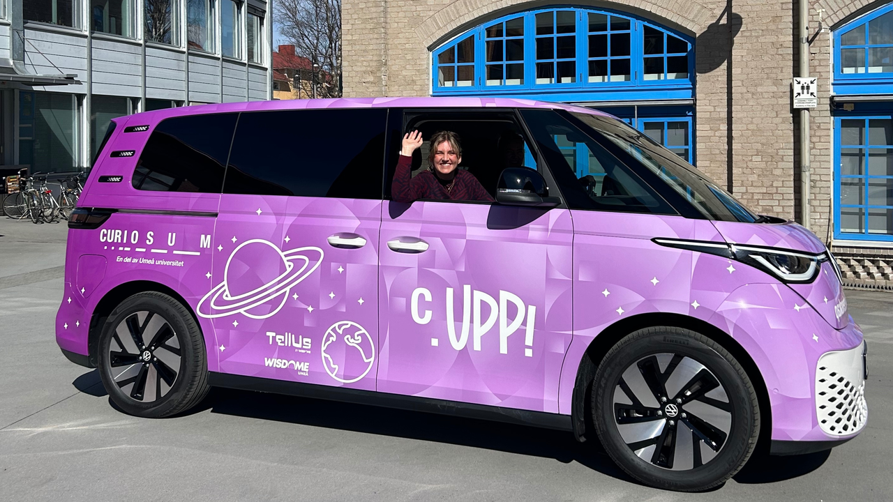 Curiosums lila skåpbil med en kvinna som vinkar ut genom fönstret.