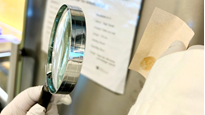 Hand som håller i ett förstoringsglas och undersöker ett fingeravtryck.