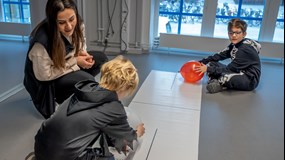 En av Curiosums besöksvärdar instruerar två besökare som skapar statisk elektricitet med ballonger.
