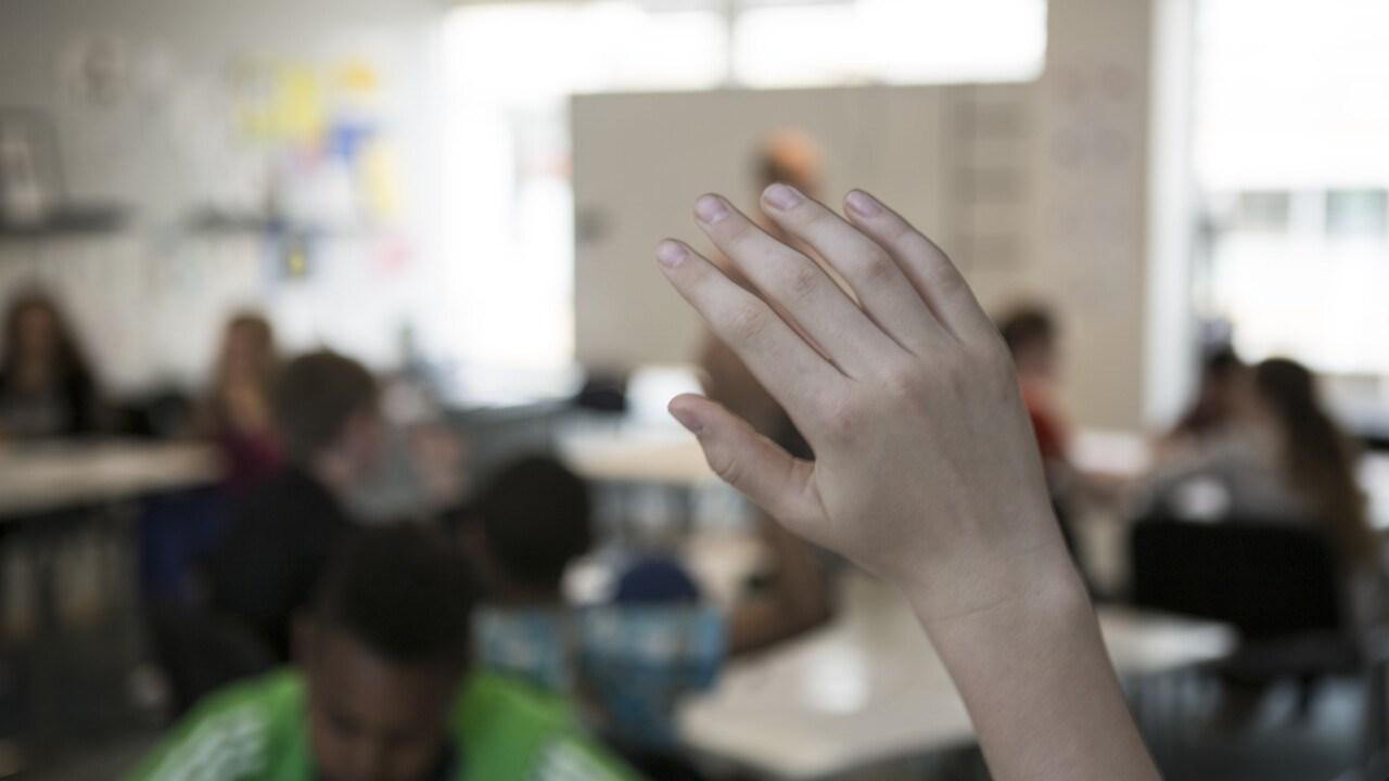 Närbild på hand på skolbarn som räcker upp handen i klassrummet.