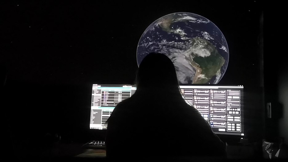 A silhouette of a man in front of the control panel in Curiosums dome. In the background the Earth on the screen.